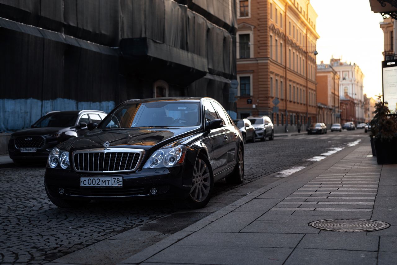 A luxurious black Maybach car parked on a cobblestone street in an urban setting at sunset.